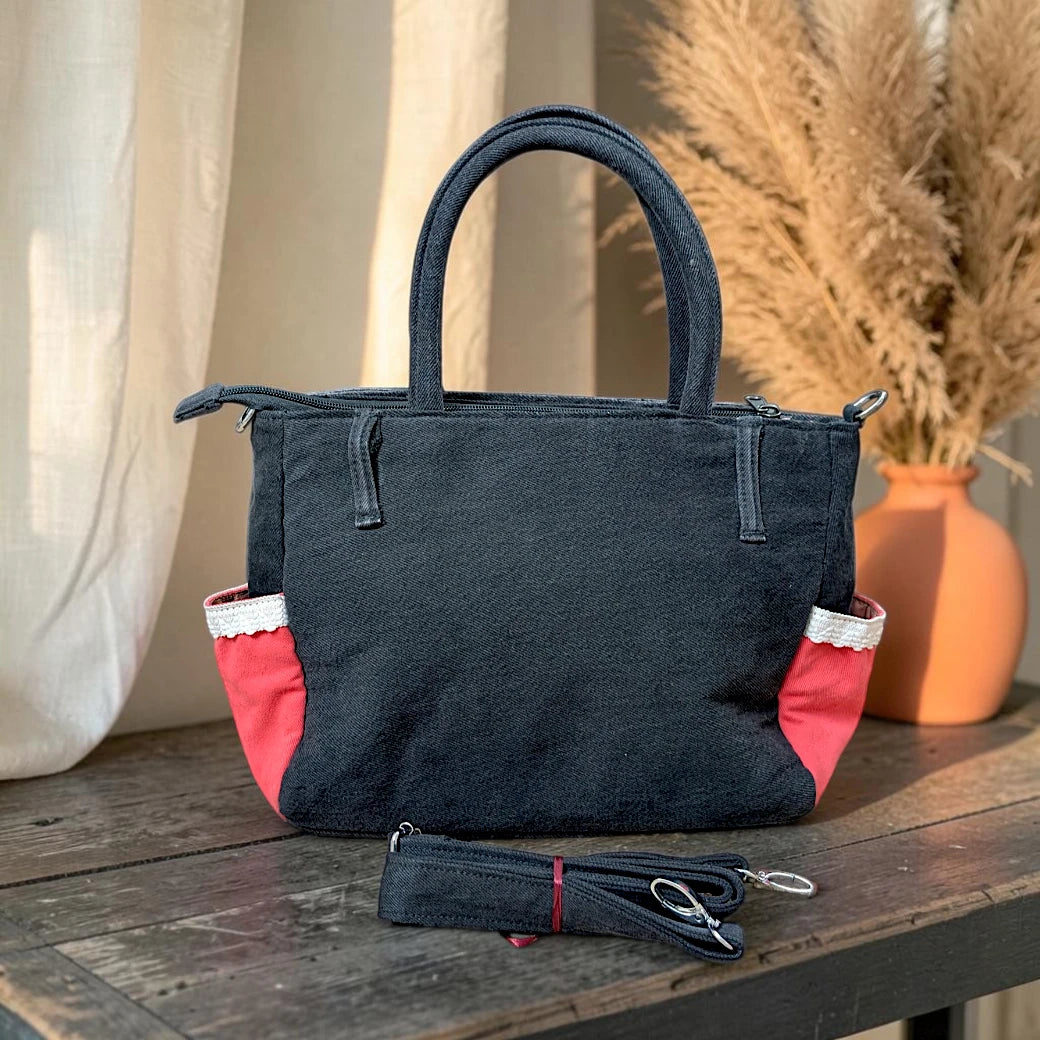 Bidora black upcycled denim handbag with red side panels, white lace trim, top handles, and detachable shoulder strap.