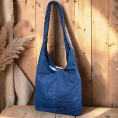 Bidora blue denim hobo shoulder bag with a slouchy silhouette and wooden toggle closure against a wooden background