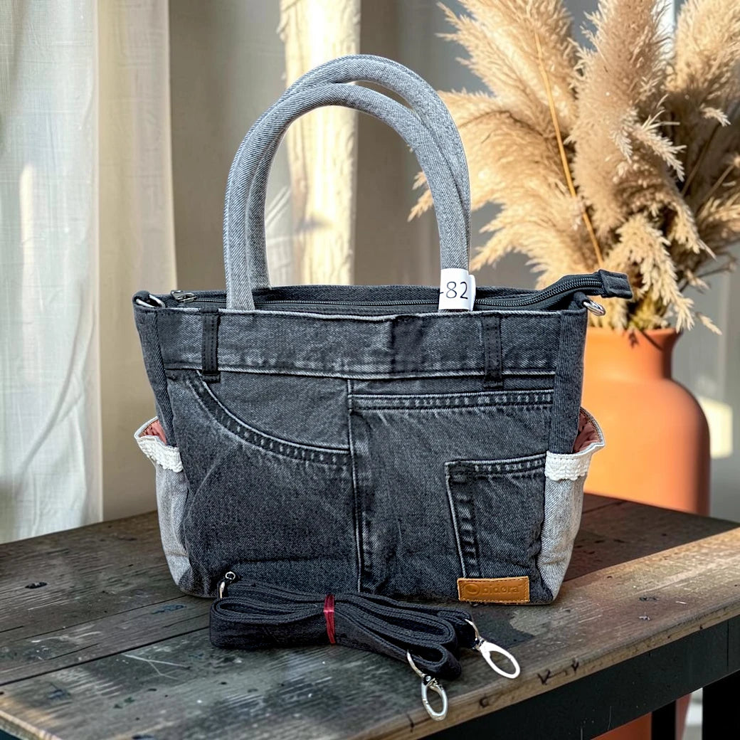 Bidora charcoal-black denim handbag with reinforced handles, exterior pockets, and a detachable shoulder strap.