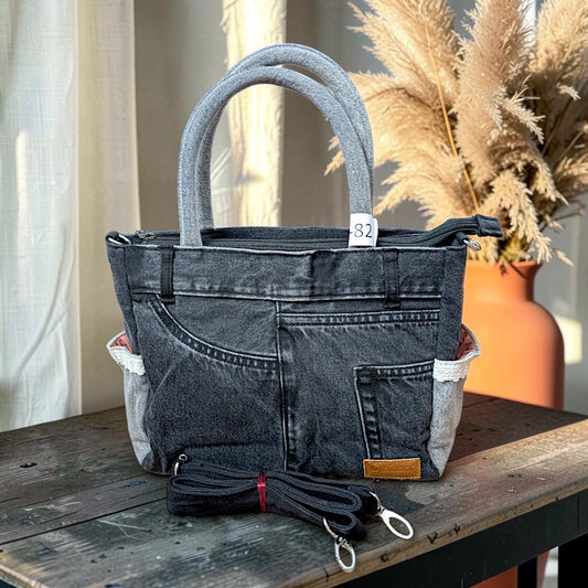 Bidora charcoal-black denim handbag with reinforced handles, exterior pockets, and a detachable shoulder strap.
