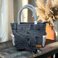 Bidora charcoal-black denim handbag with reinforced handles, exterior pockets, and a detachable shoulder strap.