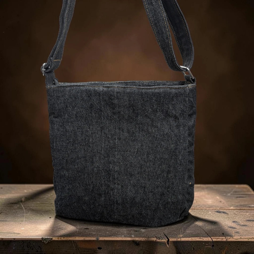 Bidora upcycled dark denim crossbody shoulder bag with an adjustable strap sitting on a rustic wooden surface.