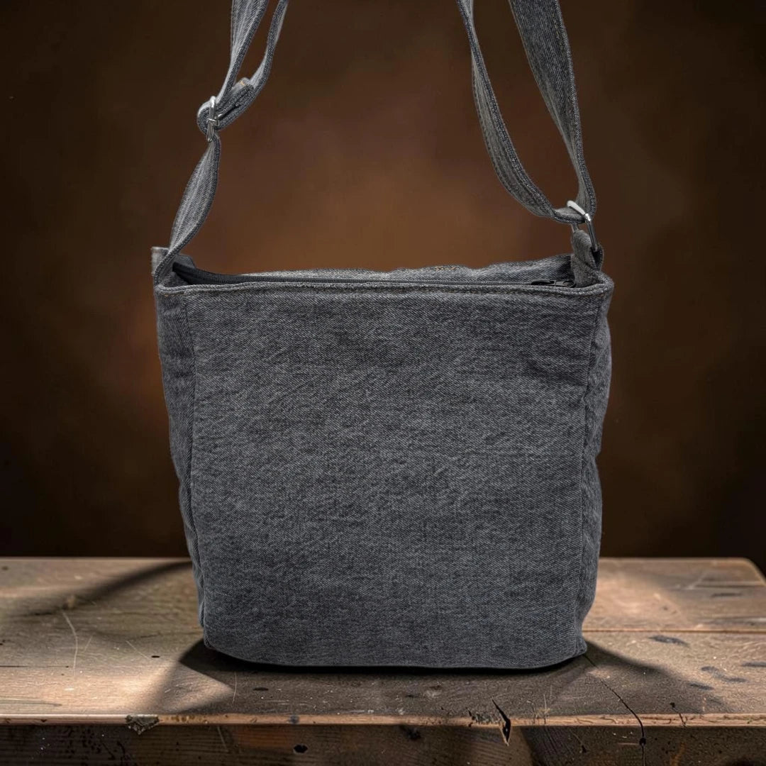 Bidora dark grey denim crossbody bag with an adjustable shoulder strap resting on a rustic wooden surface