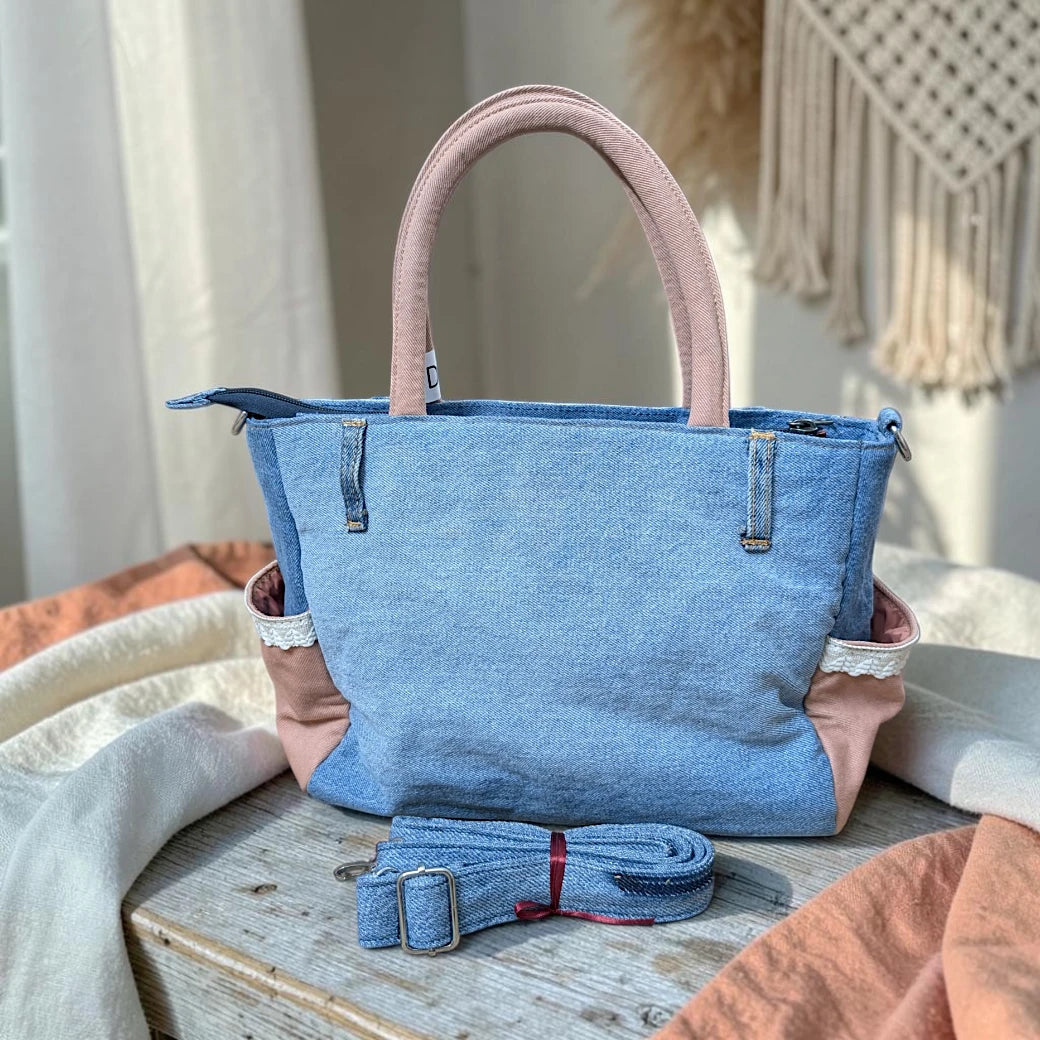 Bidora upcycled blue denim handbag with dusty rose handles, lace-trimmed side pockets, and detachable shoulder strap.