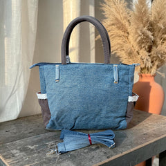 Bidora handcrafted blue denim tote bag with brown side panels, white lace trim, and a detachable shoulder strap.