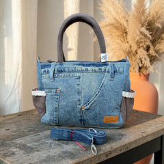 Bidora handcrafted blue denim handbag with brown accents, white lace trim, and a detachable shoulder strap on a table.