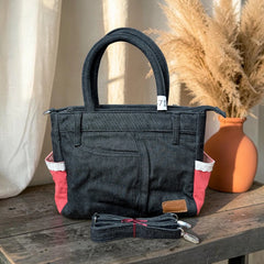 Bidora dark denim handbag with red side panels, white trim, top handles, and a detachable shoulder strap on a table.