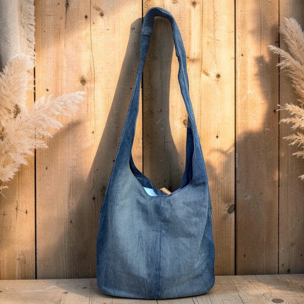 Bidora denim hobo shoulder bag with a soft-wash blue finish and a rustic wooden toggle closure against a wood background