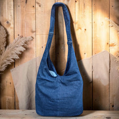 Bidora indigo denim hobo shoulder bag with a slouchy silhouette and sturdy strap against a rustic wooden background