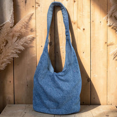 Bidora blue denim hobo shoulder bag with a slouchy silhouette and wide strap against a rustic wooden background