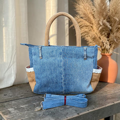 Bidora upcycled denim handbag with tan panels, lace trim, and a detachable shoulder strap on a rustic wooden table.
