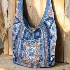 Bidora denim hobo shoulder bag with intricate hand-stitched embroidery, front pocket, and rustic wooden toggle closure.
