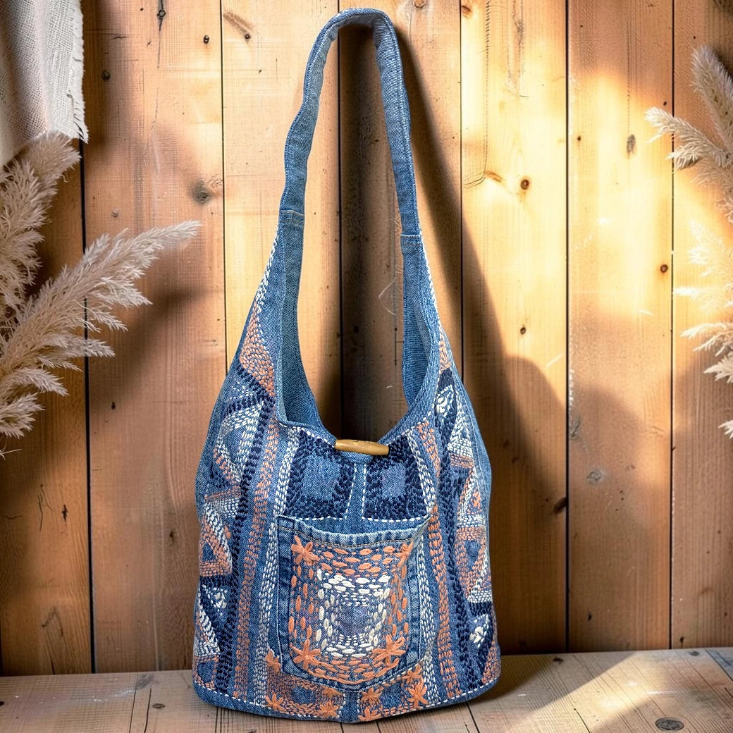 Bidora denim hobo shoulder bag with intricate hand-stitched embroidery, front pocket, and rustic wooden toggle closure.