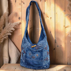 Bidora indigo denim hobo shoulder bag with intricate white hand-stitched embroidery and a rustic wooden toggle closure.