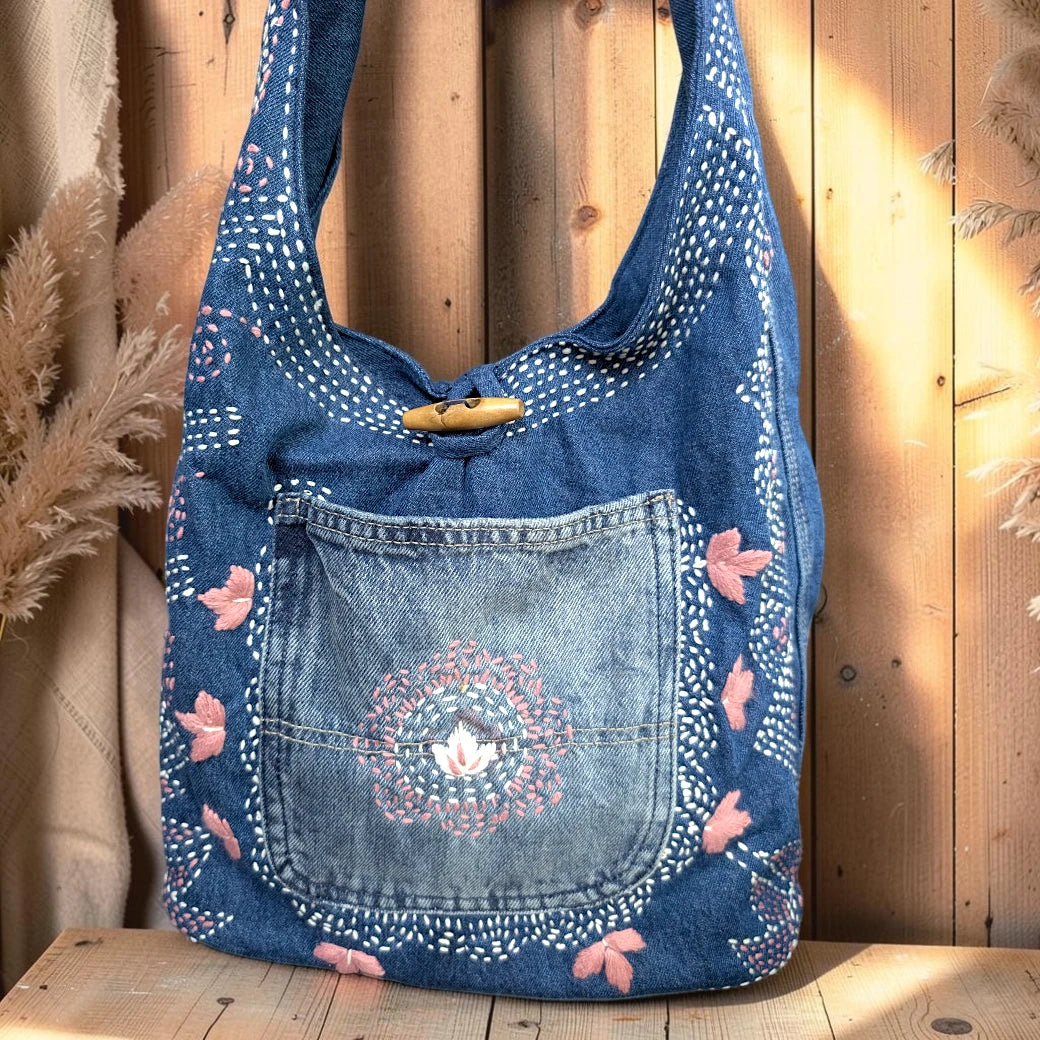 Bidora blue denim hobo bag with pink and white floral embroidery, wooden toggle closure, and front pocket.