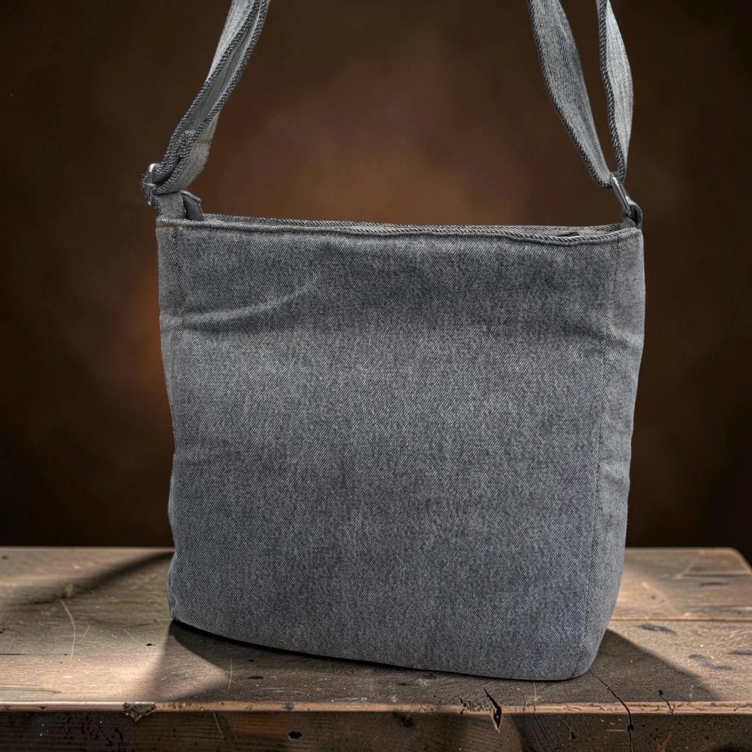 Bidora grey denim crossbody shoulder bag with an adjustable strap, displayed on a rustic wooden surface.