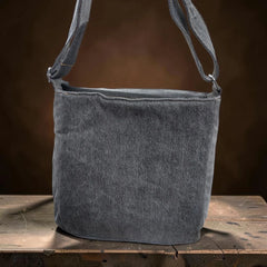Bidora grey upcycled denim crossbody shoulder bag with an adjustable strap sitting on a rustic wooden surface.