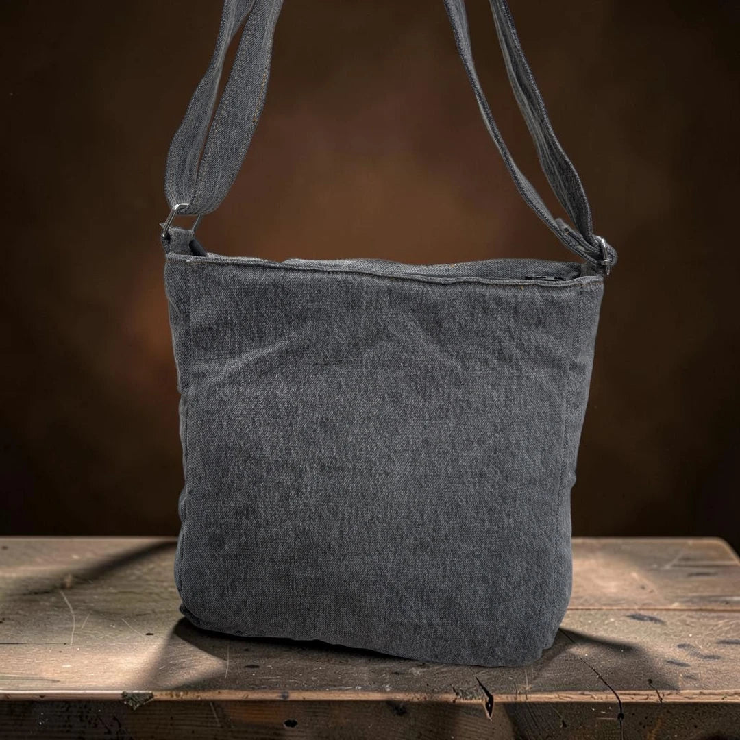 Bidora grey denim crossbody shoulder bag with an adjustable strap resting on a rustic wooden surface