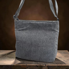 Bidora grey denim crossbody shoulder bag with an adjustable strap, displayed on a rustic wooden surface.