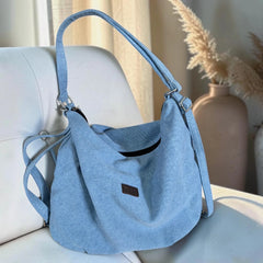 Bidora light blue denim hobo bag with an adjustable strap and secure zipper closure resting on a white chair.