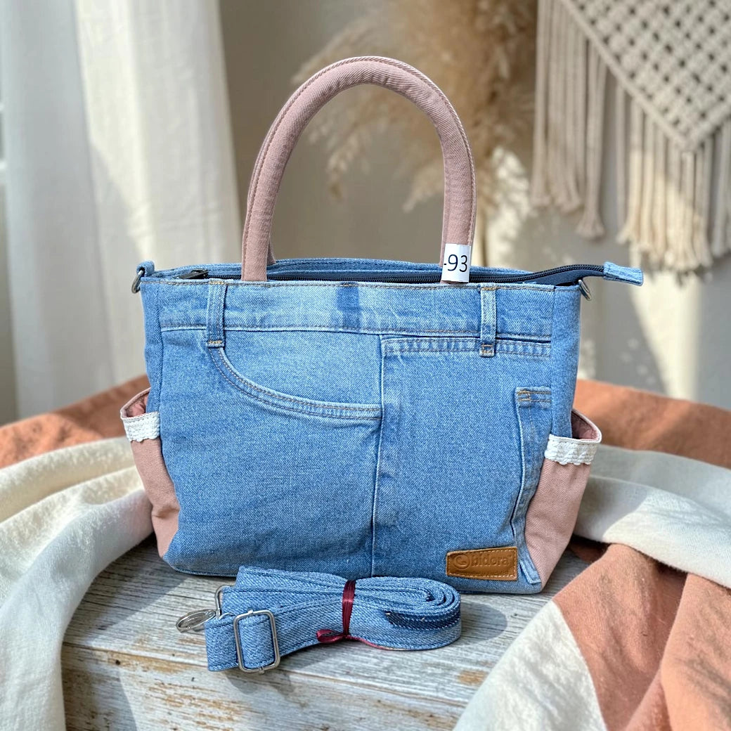 Bidora upcycled blue denim handbag with dusty rose handles, side pockets with lace trim, and detachable shoulder strap.