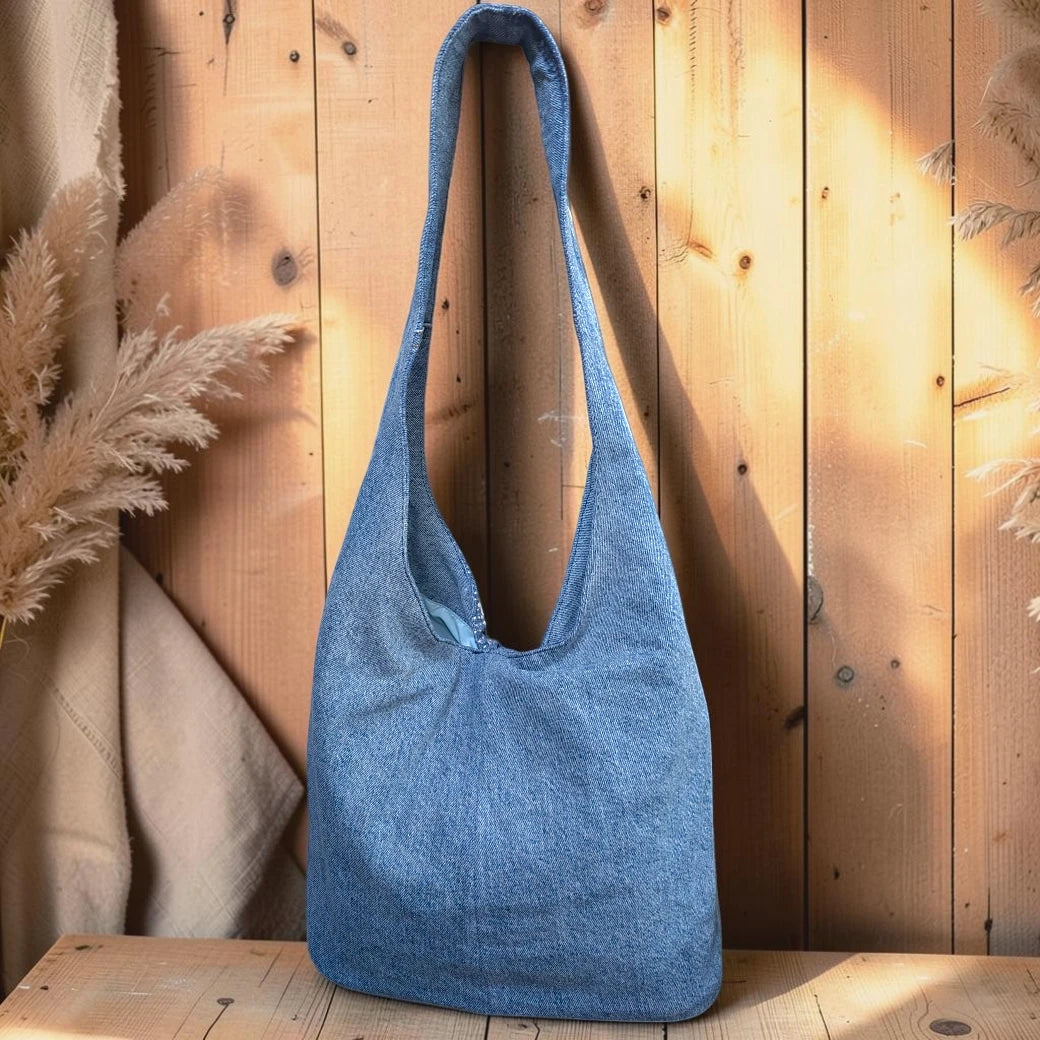 Bidora blue denim hobo shoulder bag with a slouchy silhouette and wide strap hanging against a wooden wall