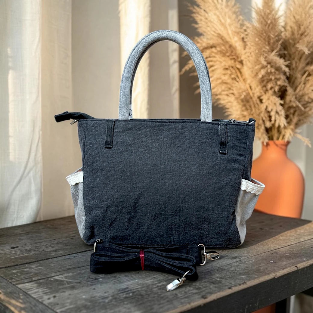 Bidora charcoal-black denim handbag with grey handles, side pockets, and a detachable black shoulder strap.