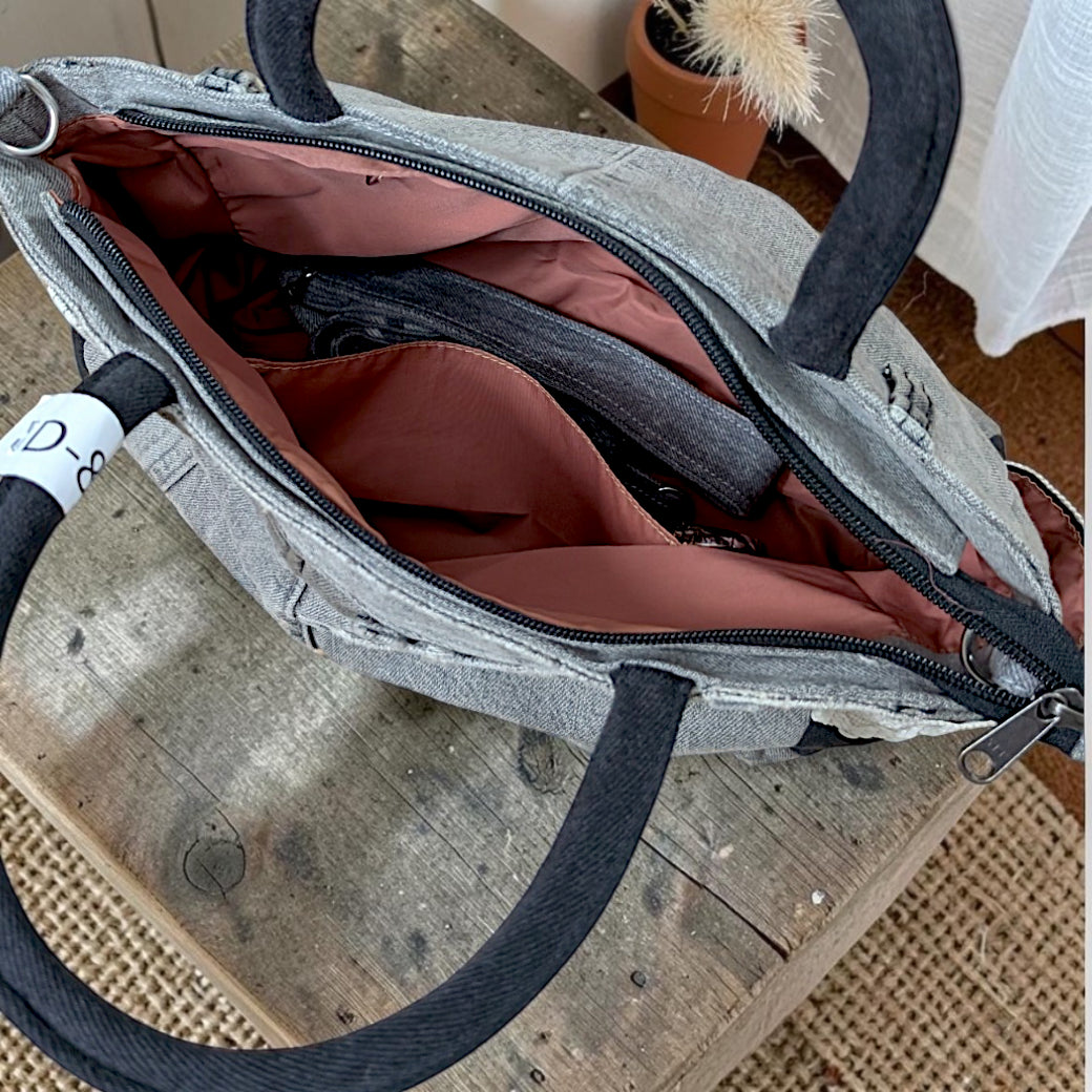 Bidora charcoal grey denim handbag with black handles and a soft pink interior lining, shown from an open top view.