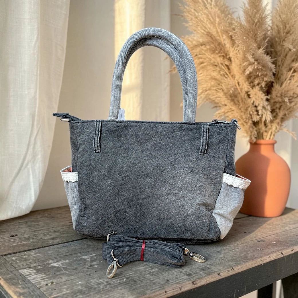Bidora charcoal grey denim handbag with side pockets, lace trim, top handles, and a detachable shoulder strap.