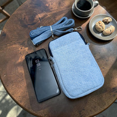 Bidora light blue denim crossbody phone pouch with detachable strap and smartphone on a rustic wooden table