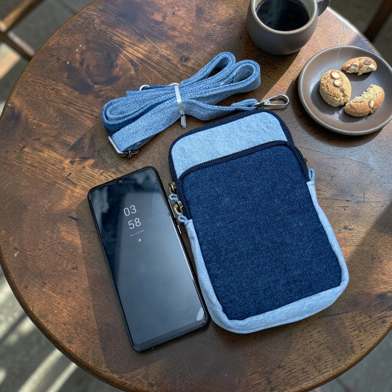 Bidora two-tone denim crossbody phone pouch with adjustable strap and smartphone on a rustic wooden table
