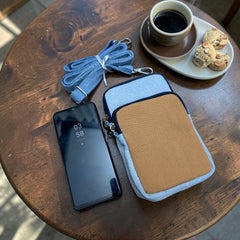Bidora casual denim crossbody phone pouch with tan pocket, adjustable strap, and smartphone on a wooden table.