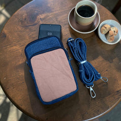 Bidora two-tone denim crossbody phone pouch with a detachable strap, resting on a wooden table next to coffee.