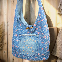 Bidora denim hobo shoulder bag with pink and white floral embroidery, exterior pocket, and wooden toggle closure.