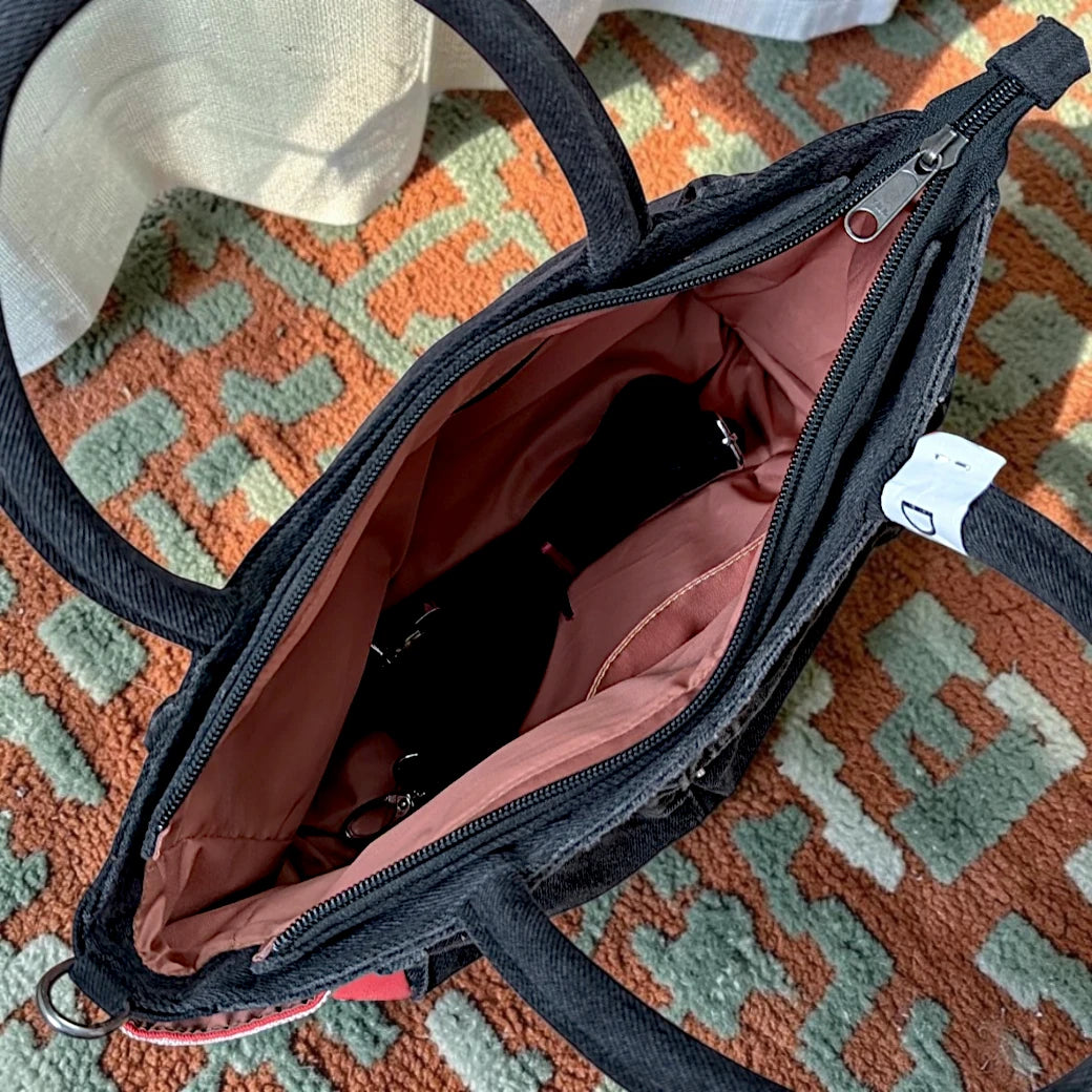 Bidora dark denim handbag with a spacious interior, zipper closure, sturdy top handles, and red side panel detail.
