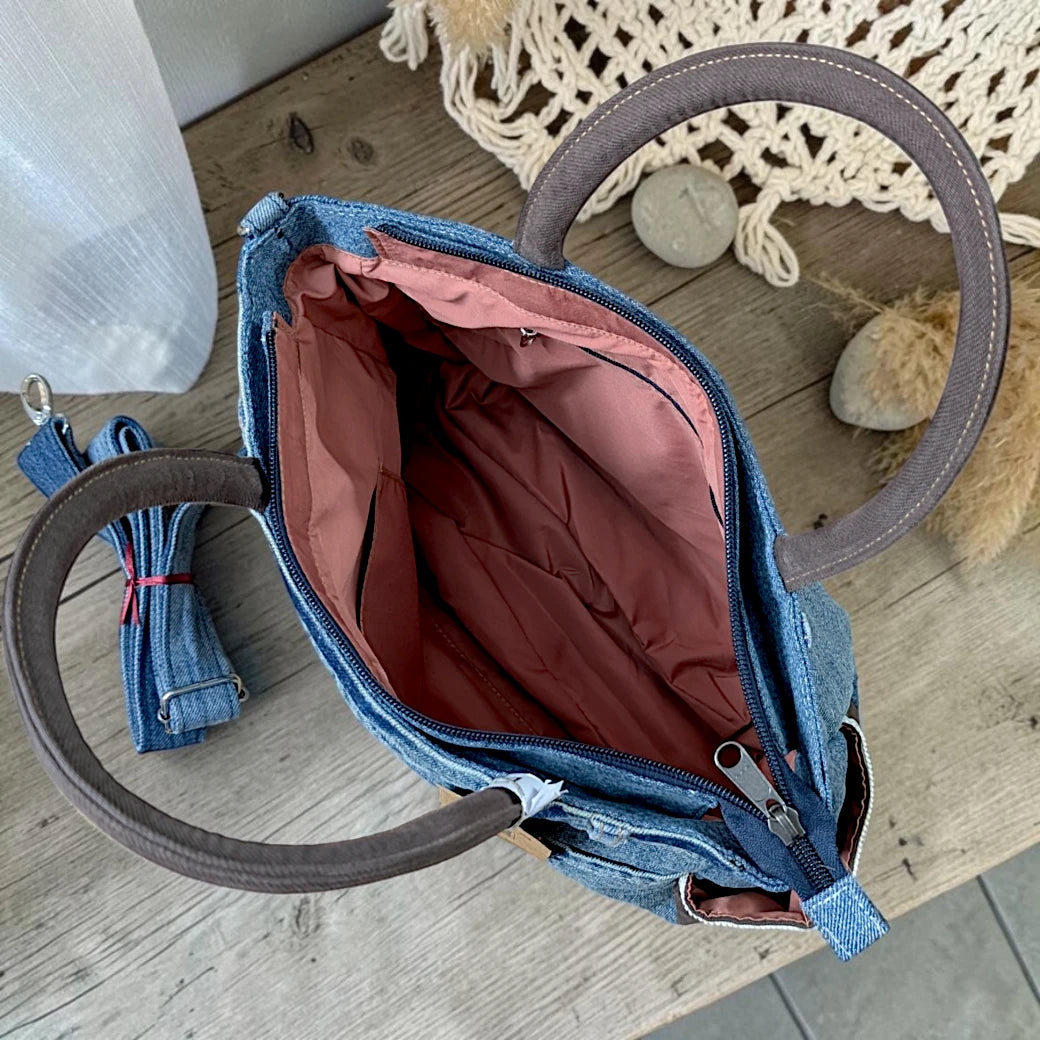 Bidora denim handbag with brown handles, zipper closure, and detachable shoulder strap on a wooden surface