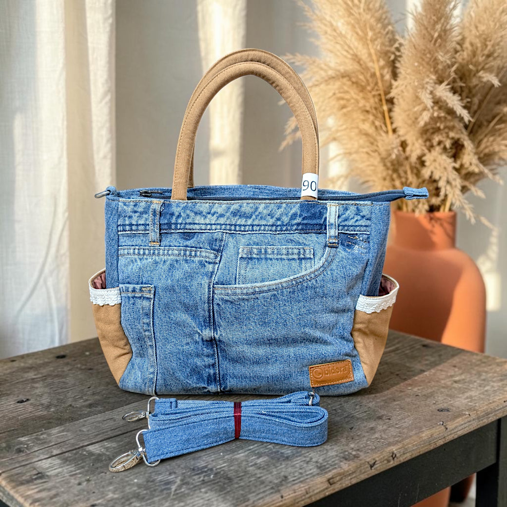 Bidora upcycled blue denim handbag with tan panels, lace trim, and a detachable shoulder strap on a wooden table.