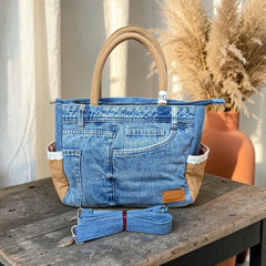 Bidora upcycled blue denim handbag with tan panels, lace trim, and a detachable shoulder strap on a wooden table.
