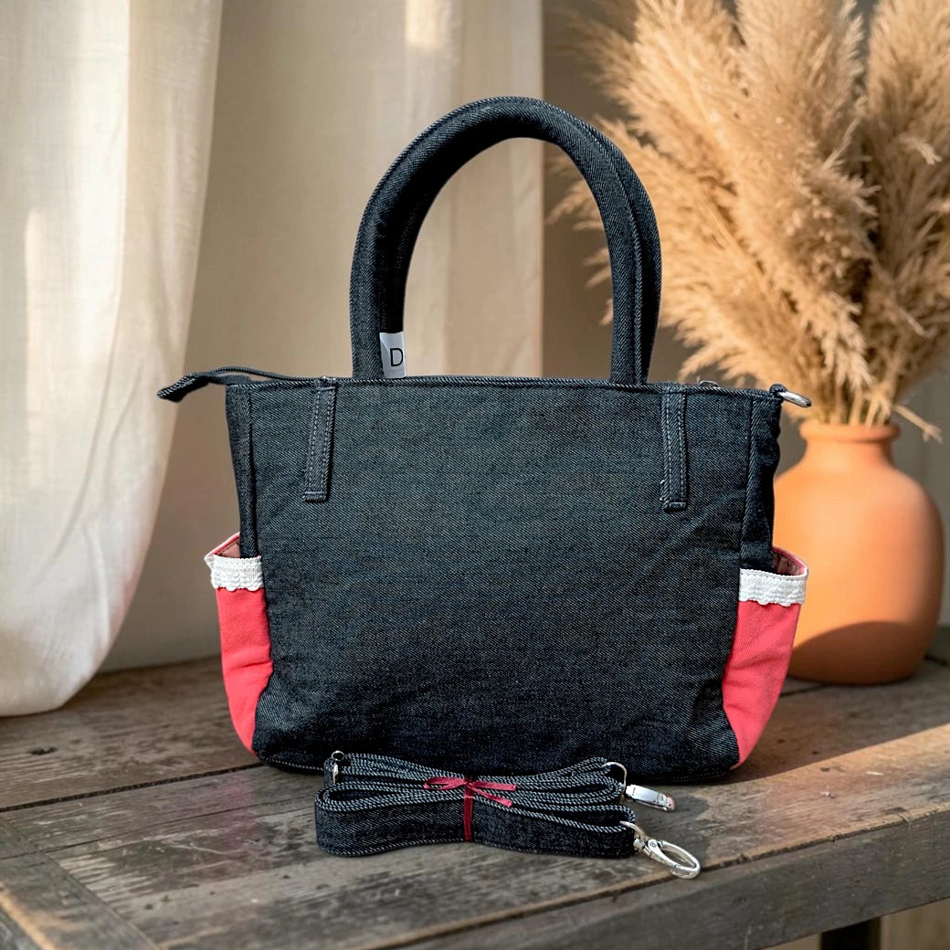 Bidora dark denim handbag with red side panels, white trim, top handles, and a detachable shoulder strap on a table.