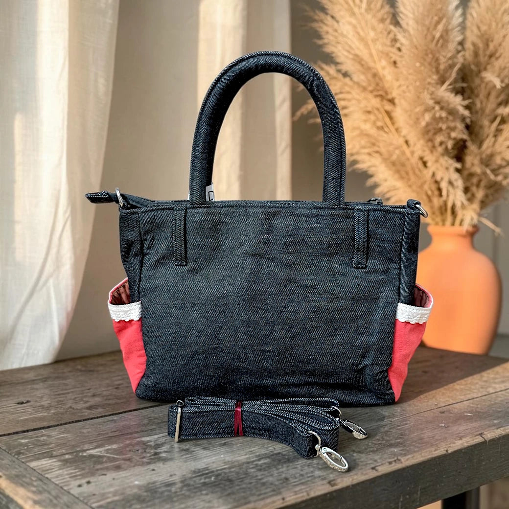 Bidora dark wash denim handbag with red side pockets, white lace trim, top handles, and a detachable shoulder strap.
