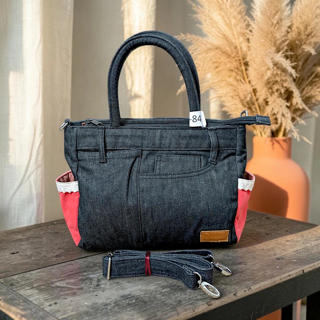 Bidora dark wash denim handbag with red side pockets, white lace trim, top handles, and detachable shoulder strap.