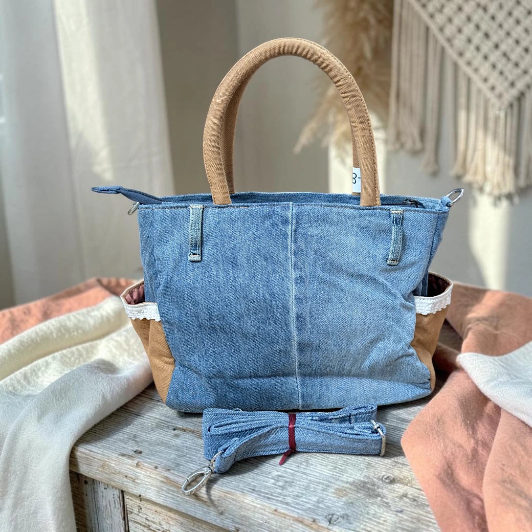 Bidora upcycled blue denim handbag with tan handles, lace trim, and a detachable shoulder strap on a rustic table.