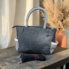 Bidora washed-grey denim handbag with lace trim, side pockets, and a detachable shoulder strap on a wooden table.