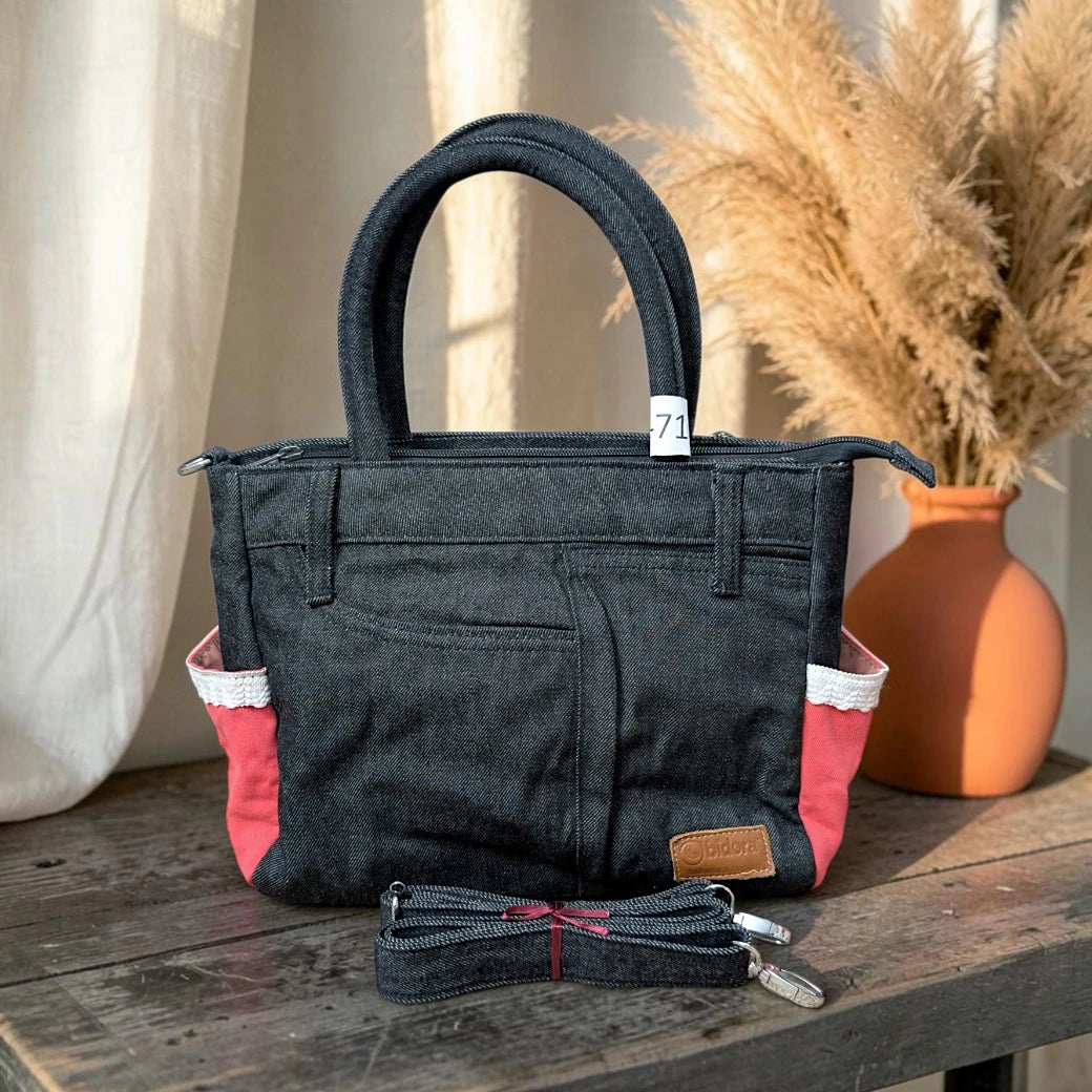 Bidora dark denim handbag with red side panels, white trim, top handles, and a detachable shoulder strap on a table.