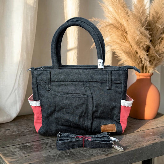 Bidora dark denim handbag with red side panels, white trim, top handles, and a detachable shoulder strap on a table.