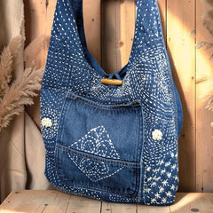 Bidora indigo denim hobo shoulder bag with white hand-stitched embroidery, exterior pocket, and wooden toggle closure.