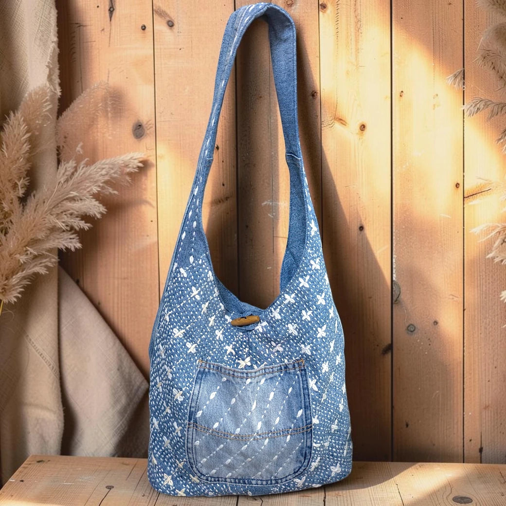 Bidora denim hobo bag with white hand-stitched embroidery, exterior pocket, and rustic wooden toggle closure.