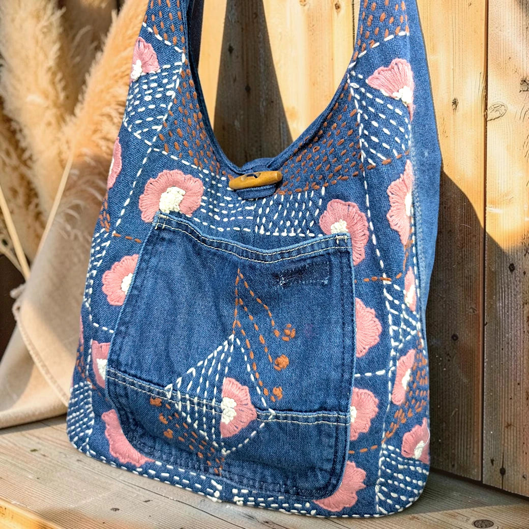 Bidora blue denim hobo shoulder bag with pink floral embroidery, kantha stitching, and a wooden toggle closure.