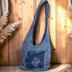 Bidora indigo denim hobo shoulder bag with white and pink hand-stitched embroidery and a rustic wooden toggle closure.