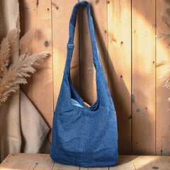 Bidora denim hobo shoulder bag with floral embroidery and wooden toggle closure against a rustic wooden background